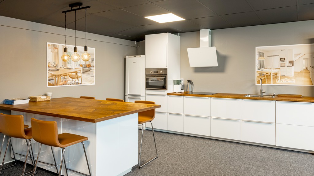 Ljust kök med vita luckor, träinslag och ett högt matbord 