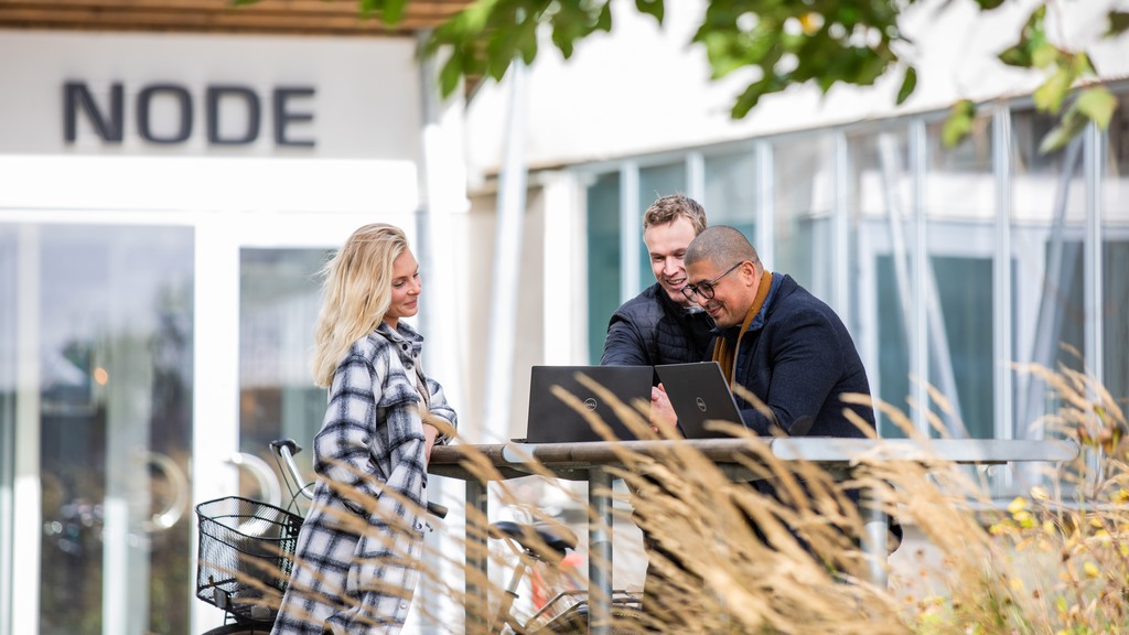 Utomhusarbete utanför fastigheten Node på Ideon i Lund. Tre personer står och kollar över två datorer vid ett högt bord.