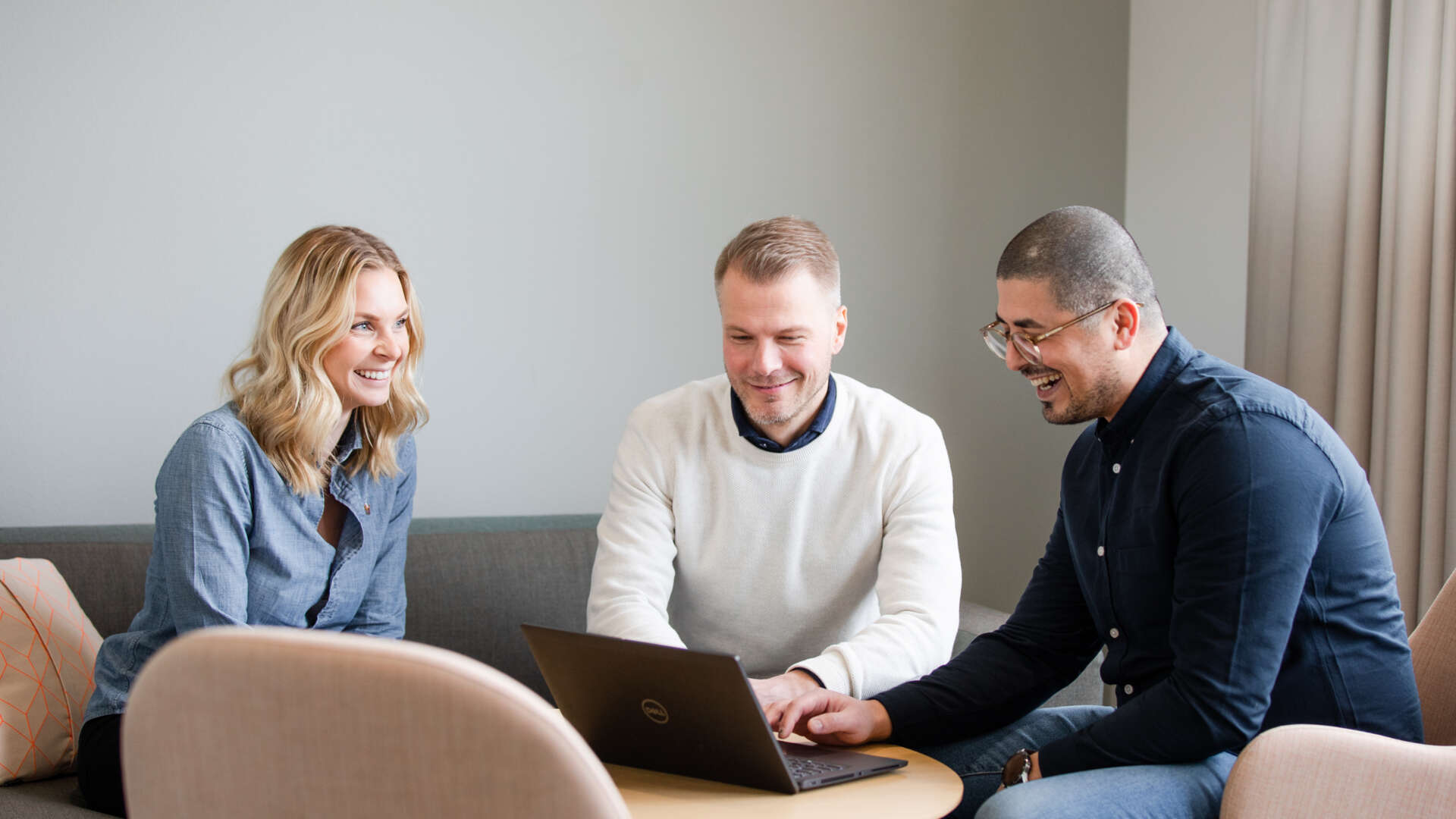 Tre personer sitter runt ett bord och tittar på en dator.