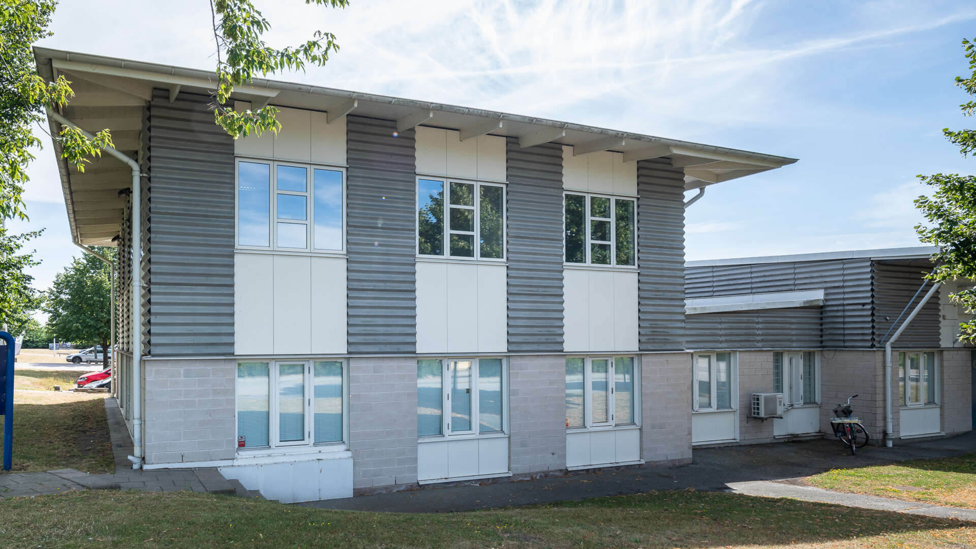 Blocket, en fastighet i två våningar med stora fönster och grönska runt om.